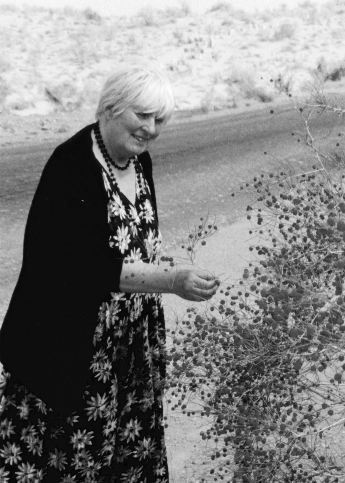 A smiling Sally among plants and flowers, holding a slender stem.